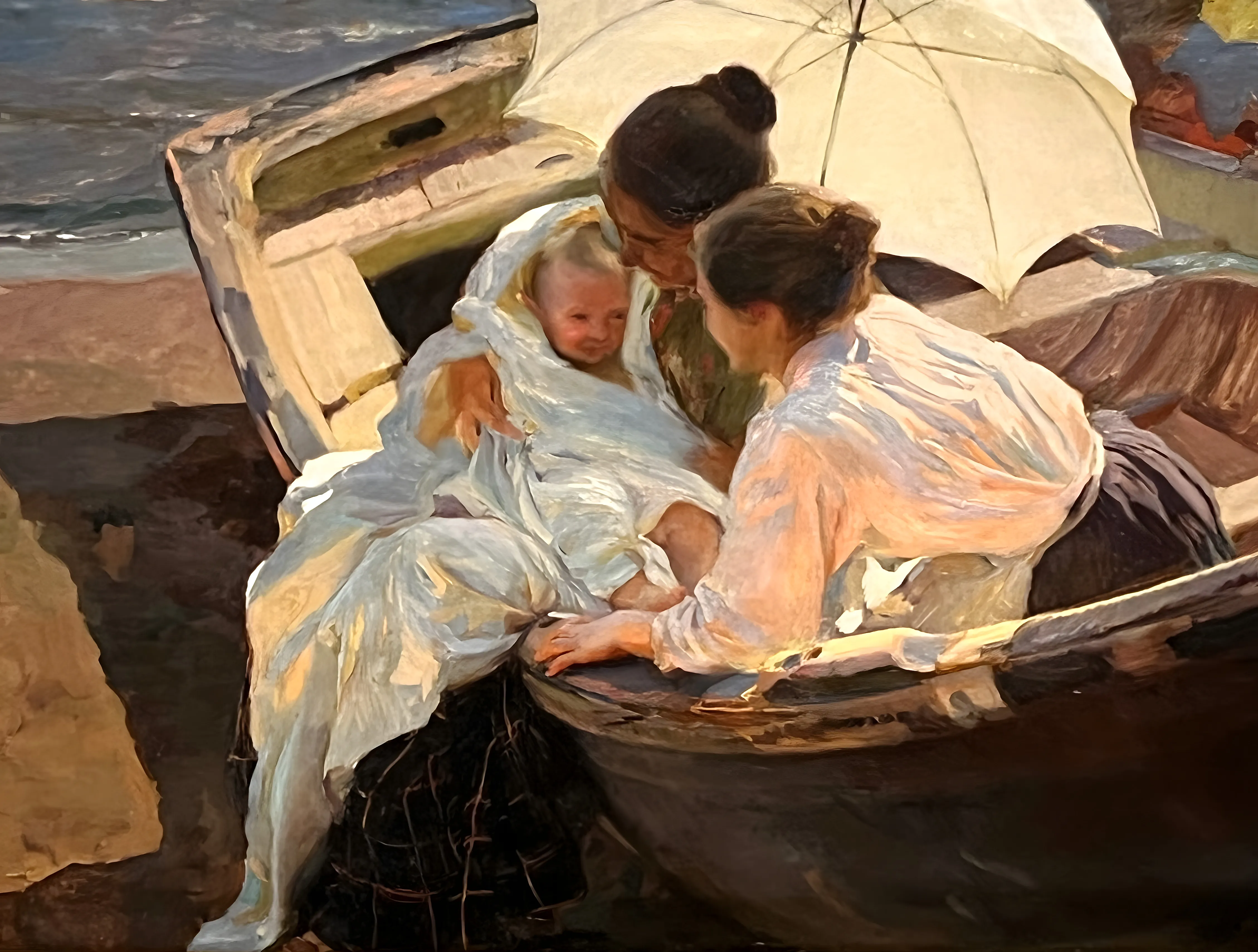 Two women in white and a freshly bathed baby wrapped in a white towel shelter beneath a cream parasol in a beached wooden boat, warm afternoon light catching the soft folds of cloth.