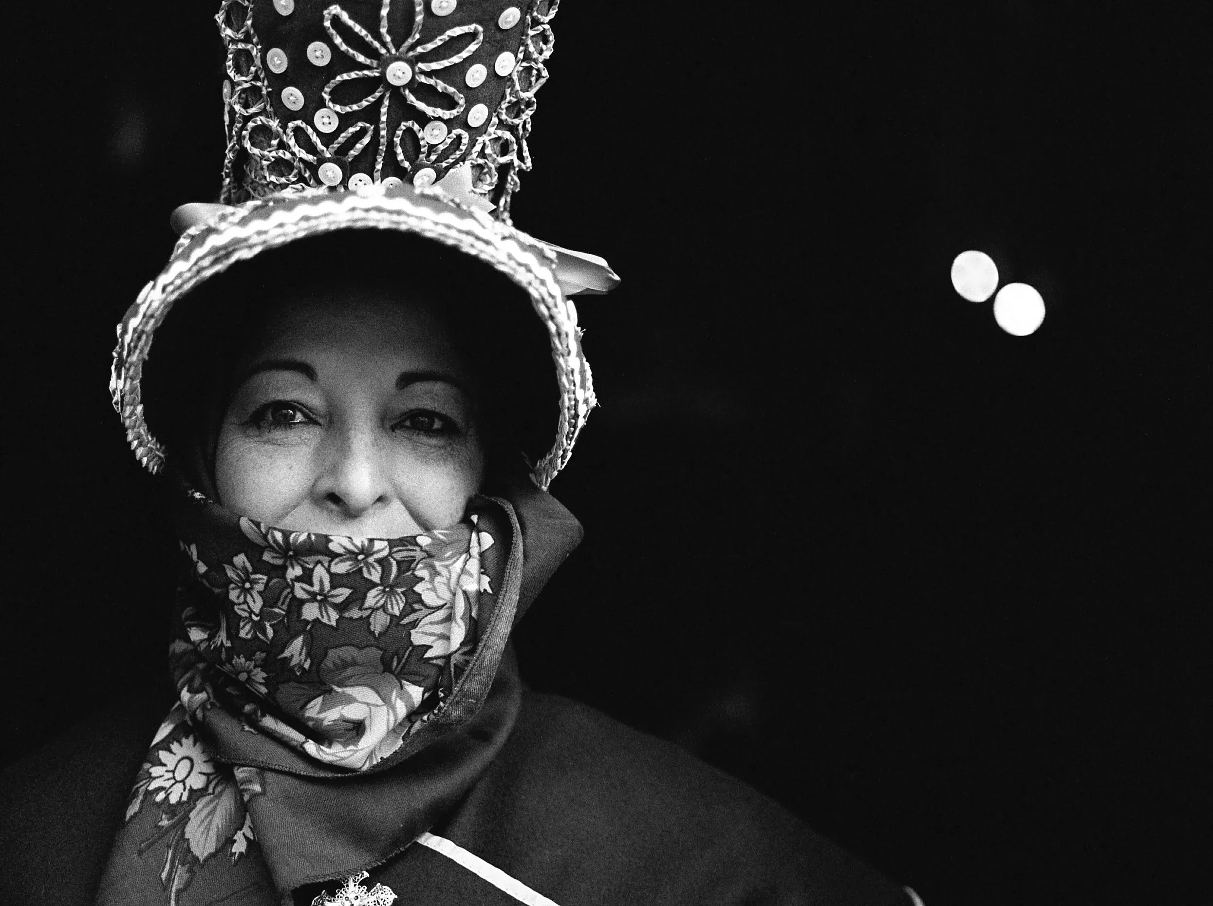 A woman in a tall, bejewelled conical festival hat and floral scarf at night, Extremadura.