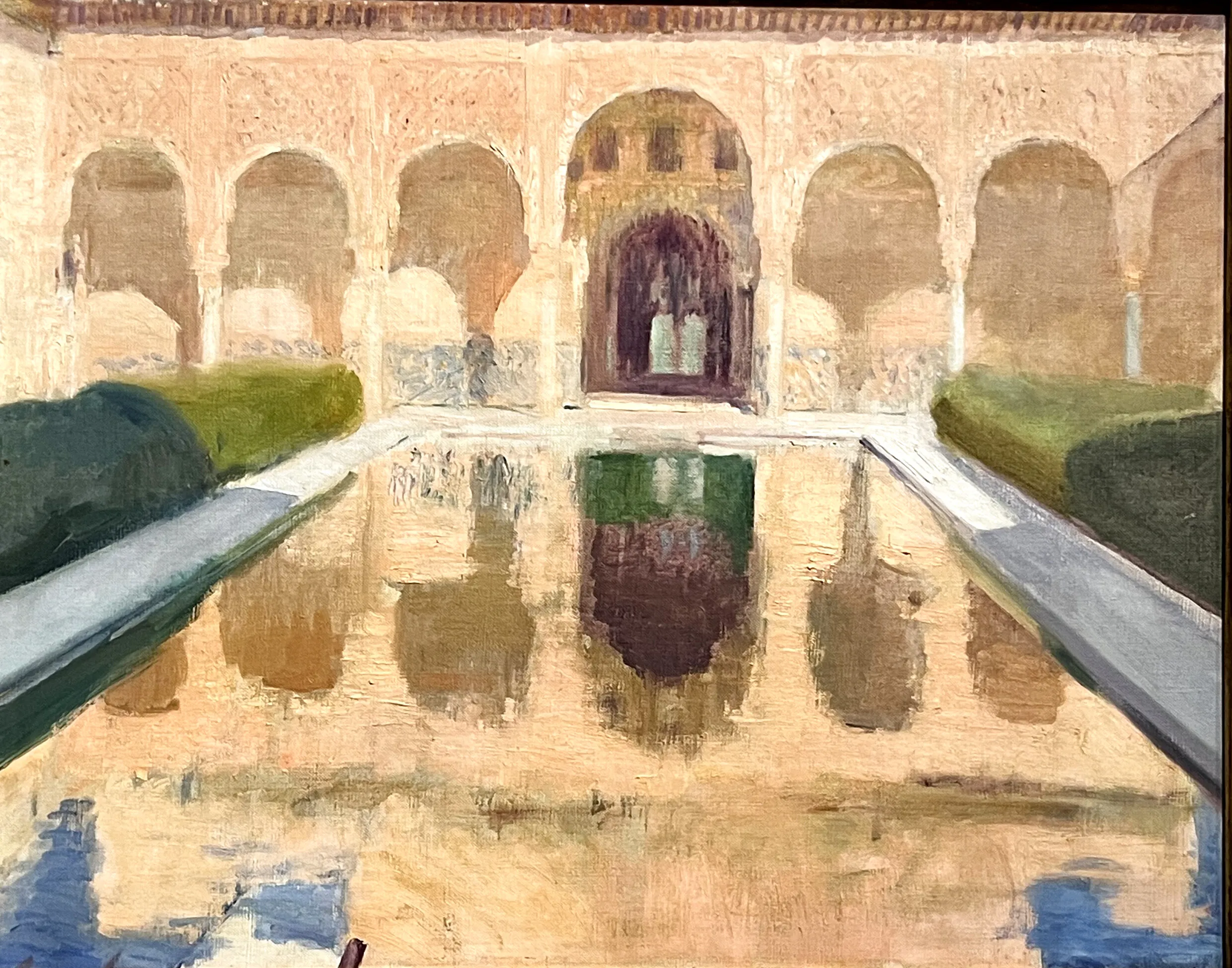 The long reflecting pool of the Alhambra's Court of the Myrtles mirrors the arched northern portico and its honey-coloured stucco, flanked by dark clipped myrtle hedges under a warm, still light.
