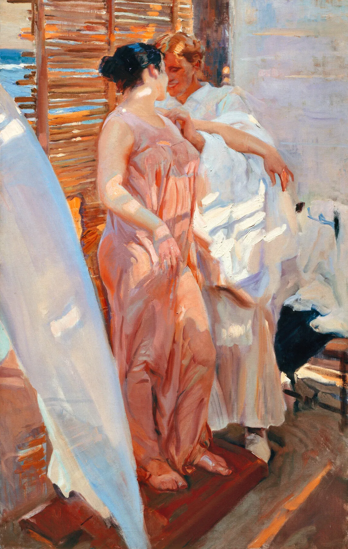 A young woman wrapped in a shimmering pink robe stands after bathing, the rose fabric glowing against a cane screen and the bright sea beyond.